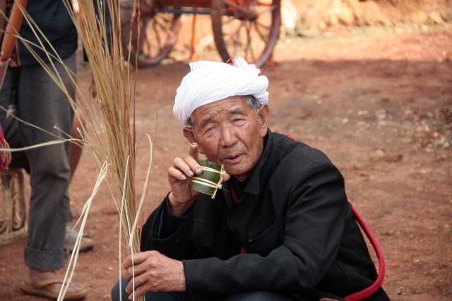 De sjamaan Loiseng Gam met zijn ceremoniele strobundel, drinkend uit ceremoniele bamboe beker.